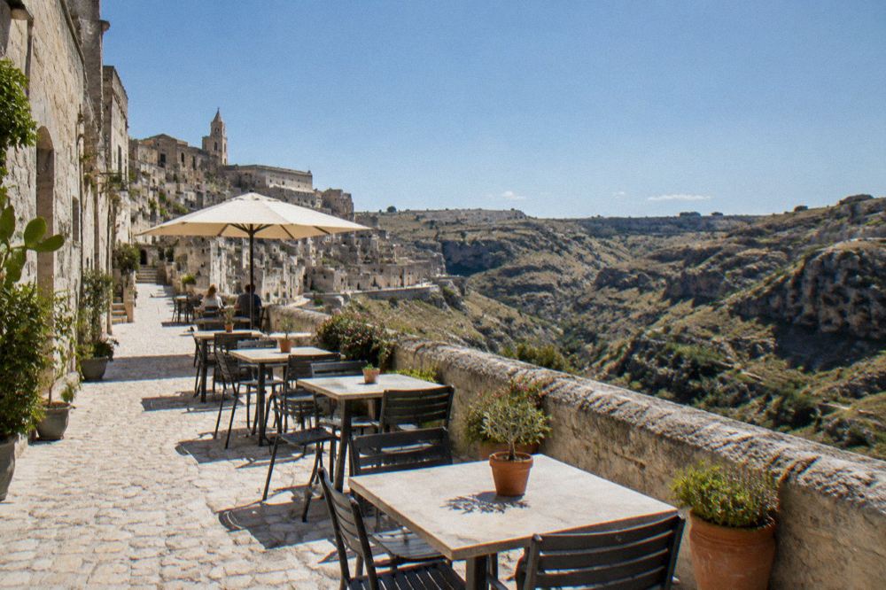 The terrace of Via Madonna delle Virtù in Matera with tables and the canyon beyond