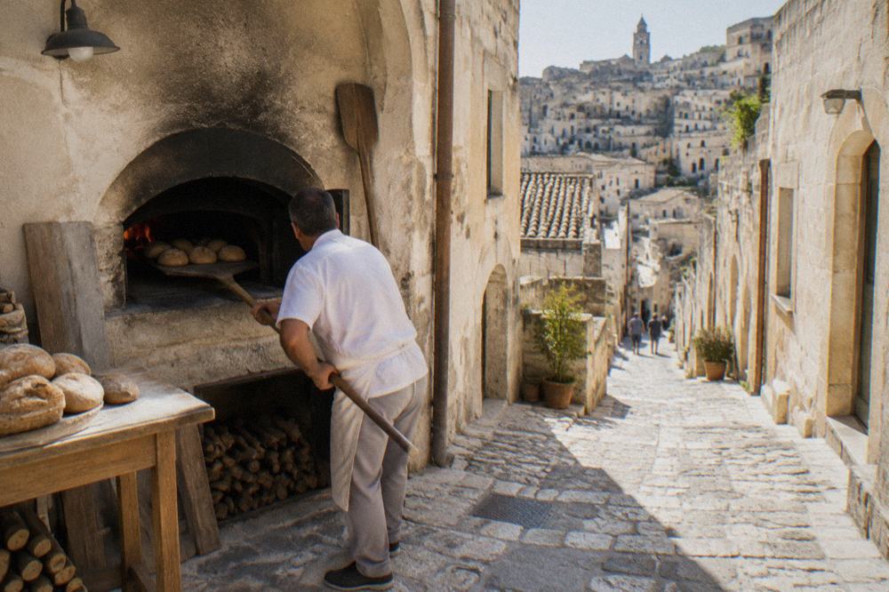 A baker sliding loaves into a wood-fired oven with a long peel