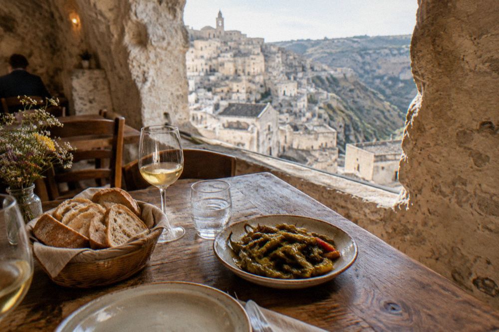 A rustic table inside a cave restaurant in Matera set with bread, wine and a dish of fried peppers