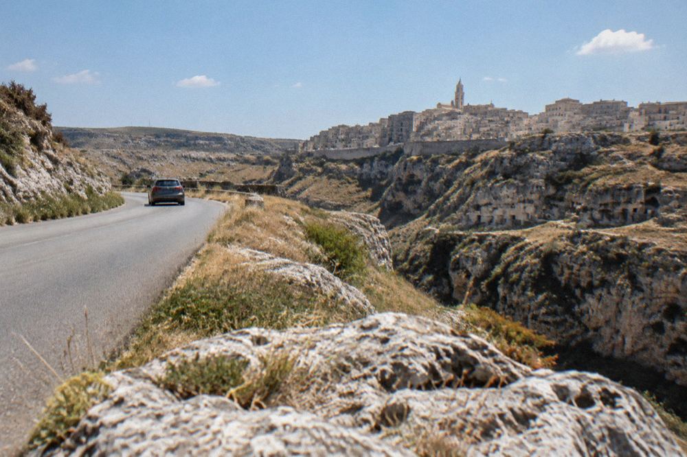 A car travelling a winding road through the bare hills of the Murgia plateau