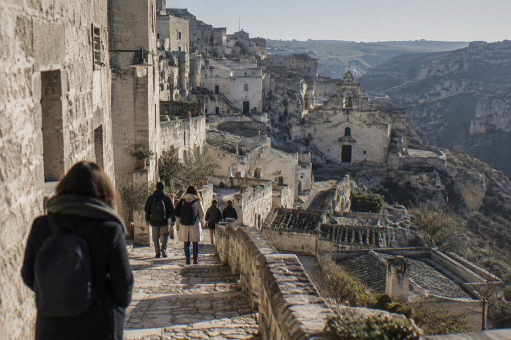 Tourists walking a narrow stepped lane between stone houses in the Sassi