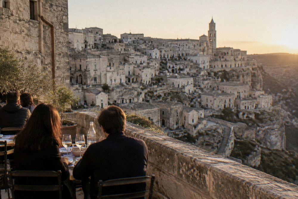 Diners at an outdoor table on a stone terrace above the Sassi at dusk