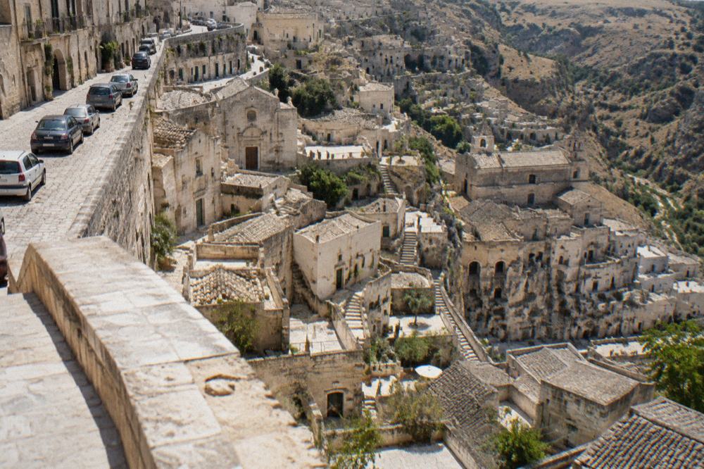 Cars parked on a street above the Sassi of Matera with the cave quarter descending below