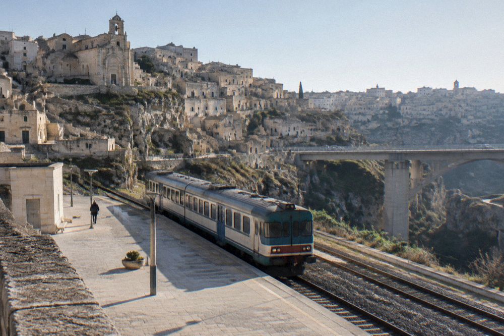 A small regional station forecourt with a diesel train waiting beside a modern road bridge