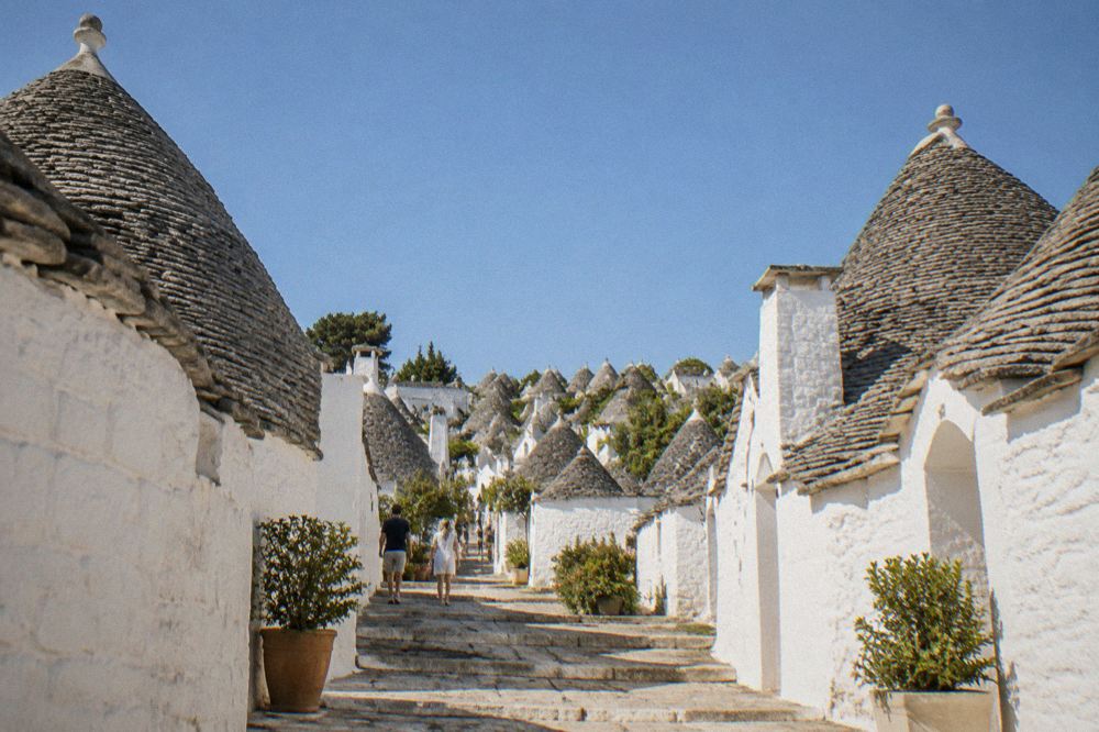Conical trulli stone dwellings with grey roofs clustered on a hillside under a clear sky