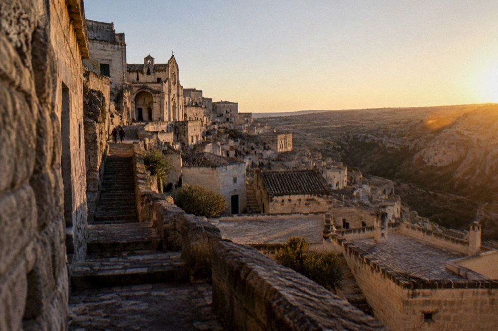 Rooftops of a stone city at dusk with a ravine and open plateau stretching to the horizon