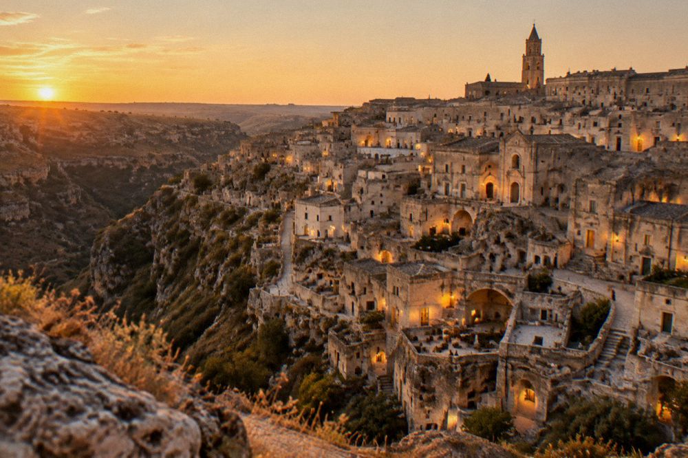 The Sassi district seen from the Murgia side of the canyon at dusk with lit windows in the cave facades
