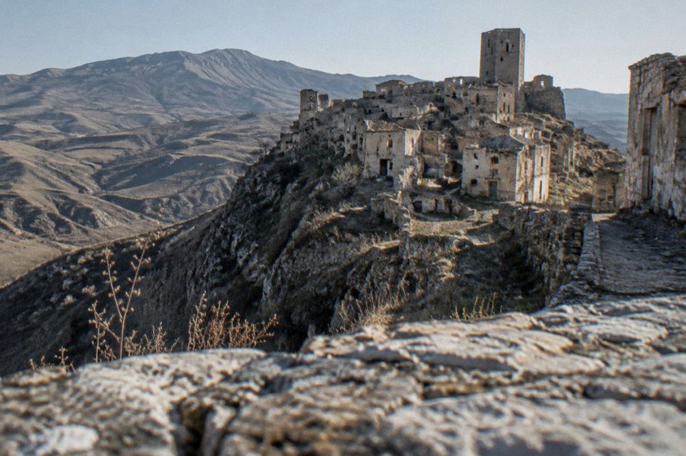 Stone houses of a mountain village clinging to a steep ridge below bare grey peaks
