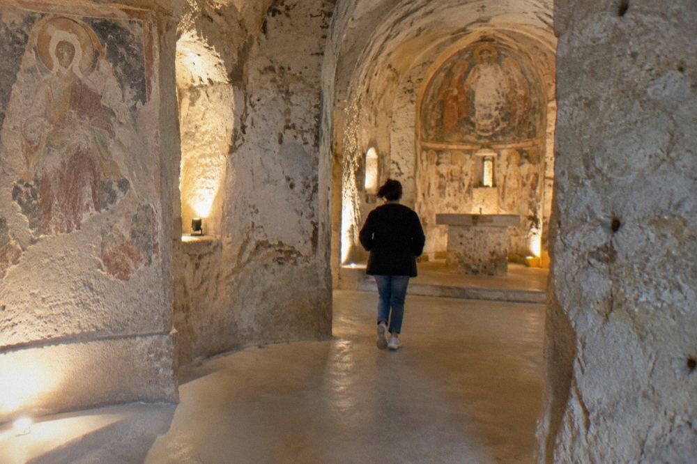 Interior of a rock-cut church in Matera with carved stone walls and soft electric lighting