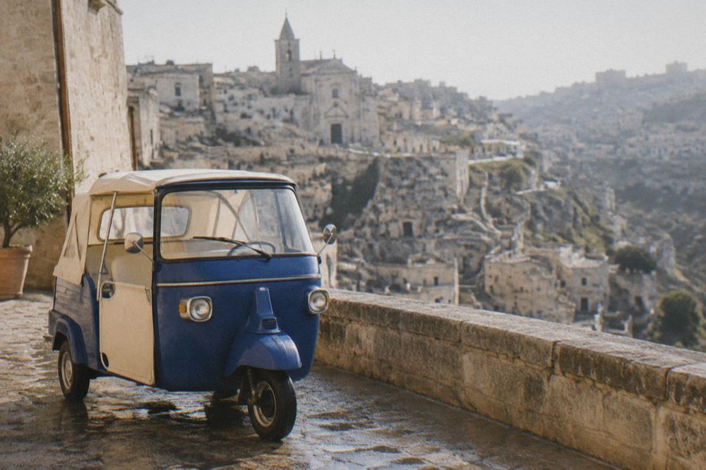 Three-wheeled Ape Calessino vehicle parked on a wet street above the Sassi of Matera