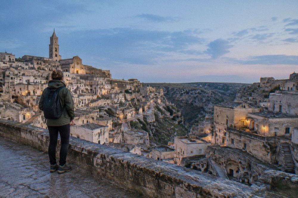 Rain jacket and sturdy walking shoes on a stone ledge overlooking wet cave rooftops in Matera