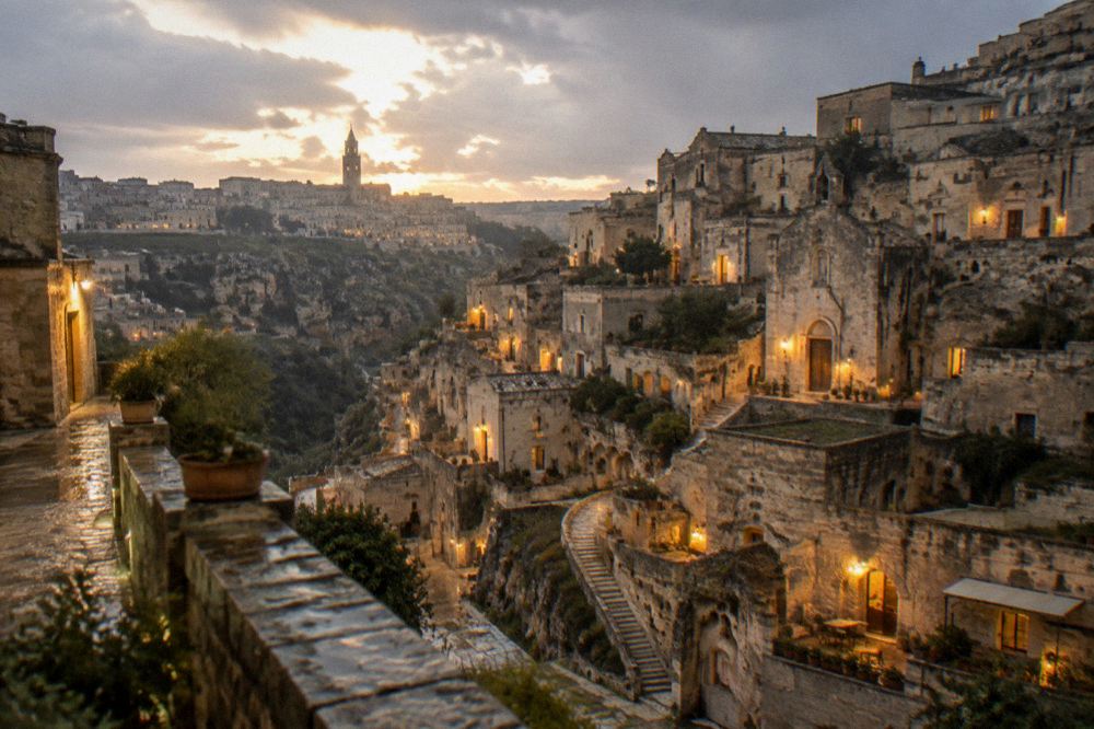 Warm lights glowing from cave-house windows in the Sassi of Matera during evening rain