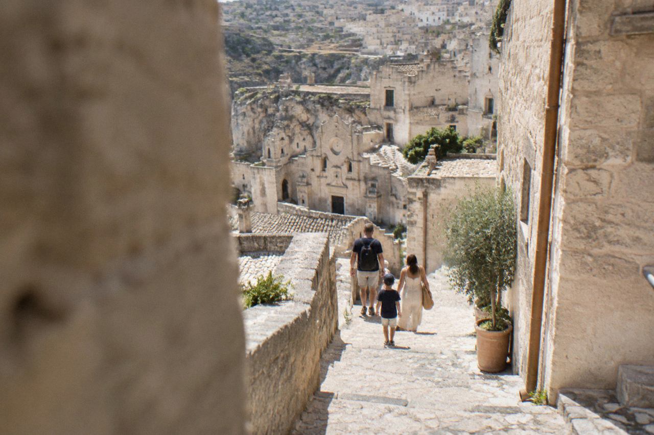 A family walking down a narrow stepped stone street between pale cave houses in the Sassi of Matera