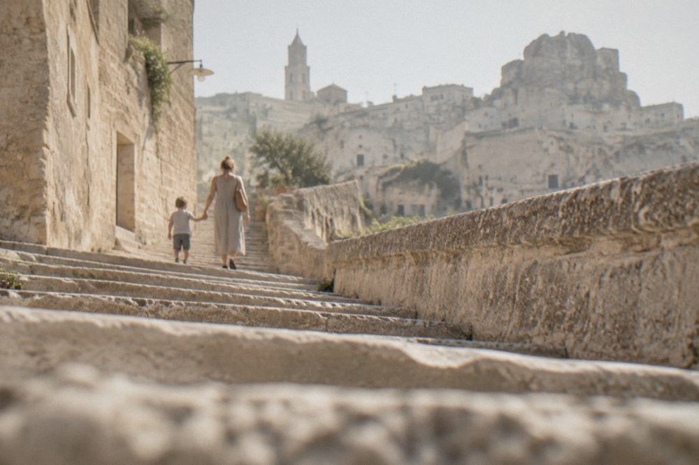 A parent holding a child's hand on a wide stone staircase between tufa buildings
