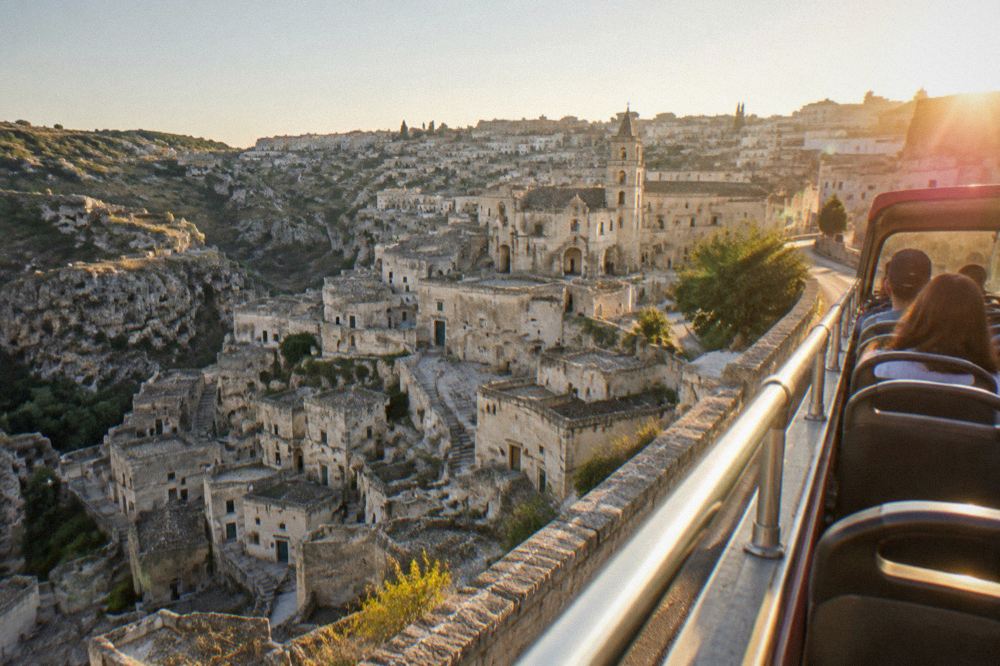 An open-top tour bus driving along a street above the Sassi at golden hour