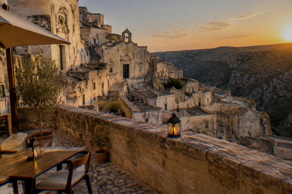 A terrace in Matera at dusk with lit lanterns and the canyon darkening behind
