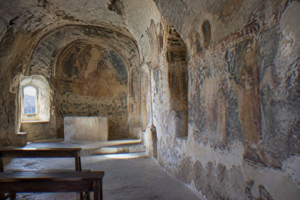 Interior of a rupestrian church in Matera with faded frescoes carved into the rock walls