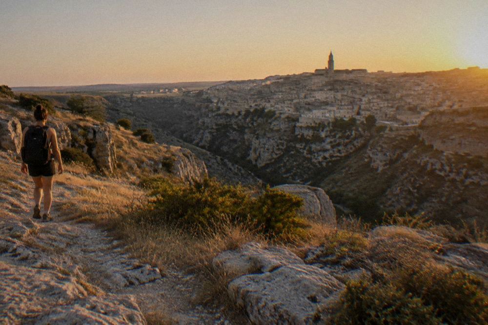 Hiker on a rocky Murgia plateau trail overlooking the Sassi of Matera across the Gravina canyon
