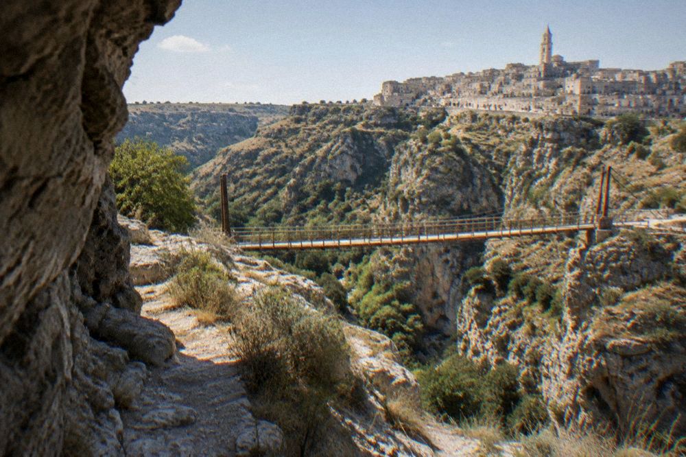 Wooden suspension bridge over the Gravina gorge seen from the rocky canyon path below the Sassi