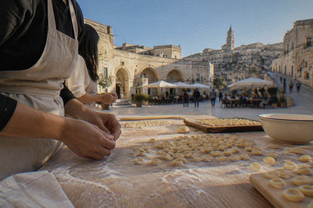 Hands shaping small pasta shapes on a floured wooden table during a cooking class