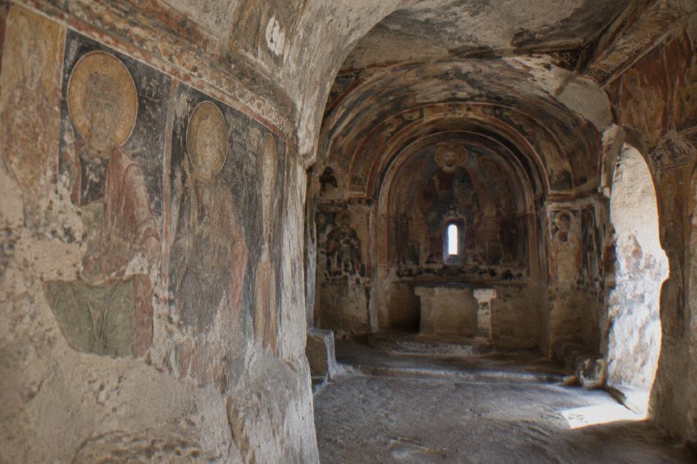 A rock-cut church interior with frescoed walls carved into the tufa stone