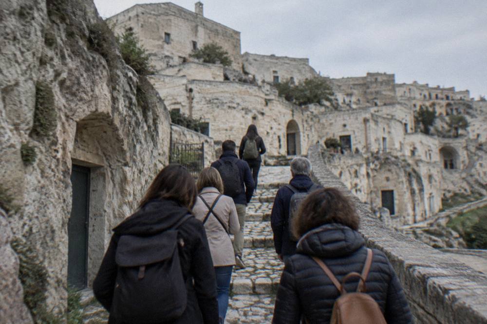 A small group of visitors seen from behind following a guide up stone steps in the Sassi of Matera